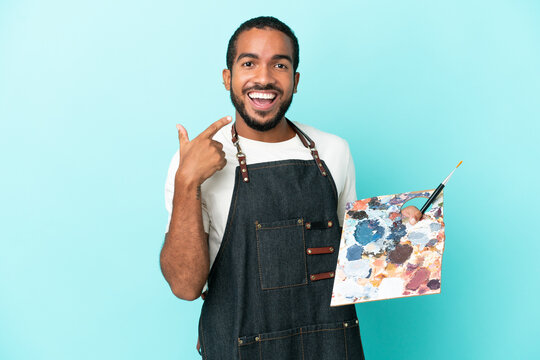 Young artist latin man holding a palette isolated on blue background giving a thumbs up gesture