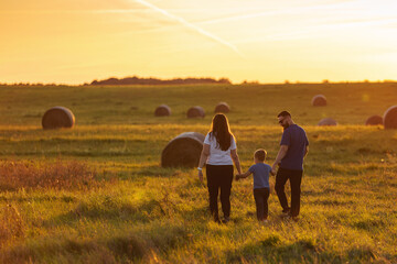Fototapeta na wymiar Mother, father and son are walking hand in hand through the wide fields of Lithuania in the evening light. A harmonious family during a walk in the fresh air