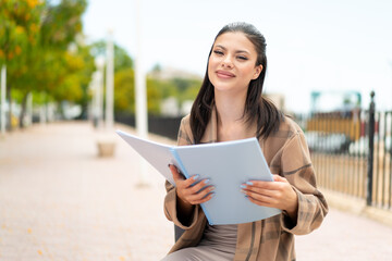 Fototapeta premium Young pretty woman at outdoors holding a notebook
