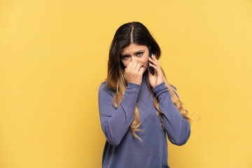 Young Russian girl using mobile phone isolated on yellow background having doubts - obrazy, fototapety, plakaty