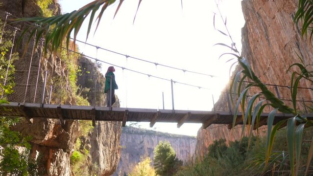 Woman walking on suspension bridge in tourist destination with huge cliffs, Chulilla.
