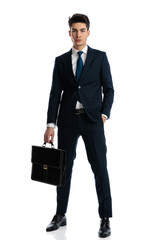 attractive young businessman holding bag and posing with hand in pocket