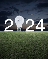 2024 white text and light bulb with wind turbine inside on green grass field over sunset sky with birds, Happy new year 2024 ecological cover concept