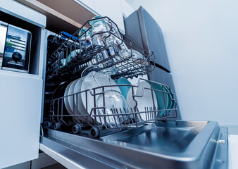 The white kitchen and opened dishwasher with clean dishes