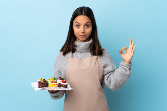 Pastry chef holding a big cake over isolated blue background in zen pose.