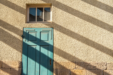 Türkisfarbene Holztüre an Mauer mit grobem Verputz mit diagonalem Schattenwurf
