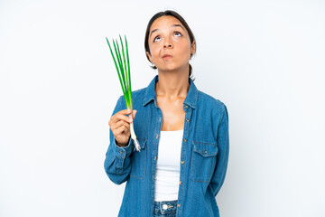 Young hispanic woman holding chive isolated on white background and looking up