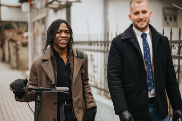 Fototapeta premium Two cheerful young multiracial business colleagues enjoying a light moment together as they walk with an electric scooter.