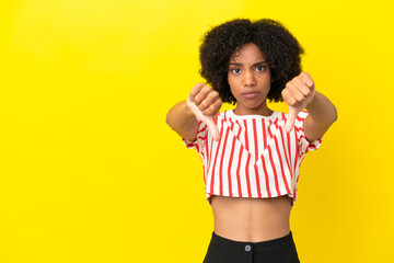 Young African American woman isolated on yellow background showing thumb down with two hands