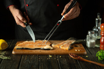 The chef prepares the fish on the kitchen table and then prepares the barbecue steak with aromatic spices. Fork and knife in the hands of the cook