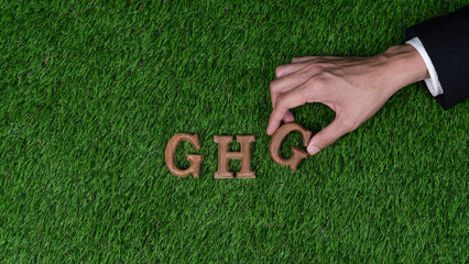 Hand arrange wooden alphabet text in GHG on biophilic green grass background as eco symbol for...