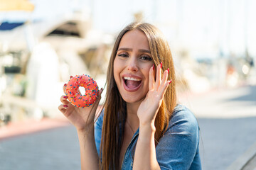Young woman holding a donut at outdoors shouting with mouth wide open