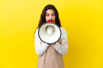 Young caucasian restaurant waiter isolated on yellow background shouting through a megaphone