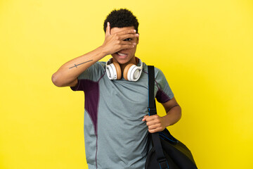 Young sport African American man with sport bag isolated on yellow background covering eyes by...
