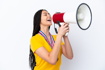 Teenager girl with braids and medals over isolated pink background shouting through a megaphone