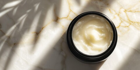 Wide banner displaying an open jar of moisturizer on a marbled surface with natural light casting shadows with copy space for make up industry and beauty salons 