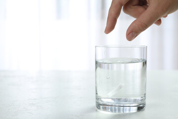Woman putting tablet into glass of water indoors, space for text