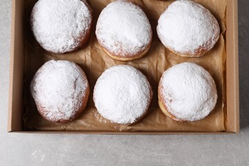 Fototapeta na wymiar Delicious buns with powdered sugar in box on light grey table, top view