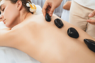 Obraz na płótnie Canvas Hot stone massage at spa salon in luxury resort with day light serenity ambient, blissful couple customer enjoying spa basalt stone massage glide over body with soothing warmth. Quiescent