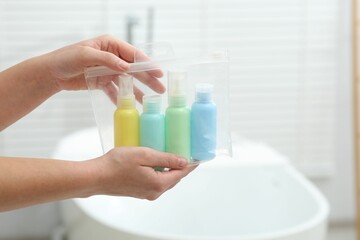 Woman with plastic bag of cosmetic travel kit in bathroom, closeup and space for text. Bath accessories