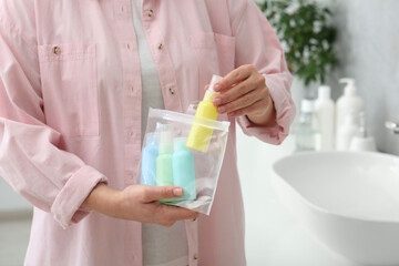 Woman packing cosmetic travel kit in bathroom, closeup. Bath accessories