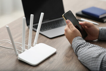 Man with smartphone and laptop connecting to internet via Wi-Fi router at wooden table, closeup