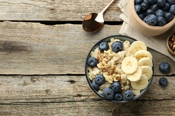 Tasty oatmeal with banana, blueberries and walnuts served in bowl on wooden table, flat lay. Space...