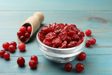 Tasty dried cranberries in bowl and fresh ones on light blue wooden table, closeup