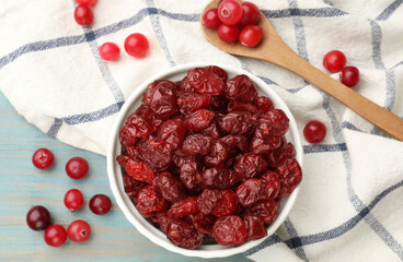 Tasty dried cranberries in bowl and fresh ones on light blue wooden table, top view