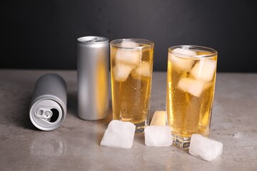 Tasty energy drink with ice cubes in glasses and aluminium cans on grey table