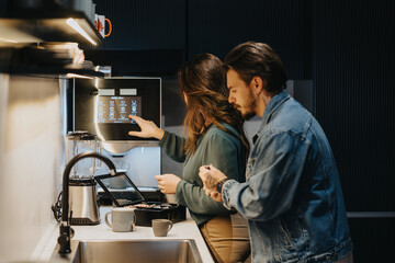 Young colleagues enjoying a relaxing morning in the office kitchen, preparing tea and having happy conversations before work.