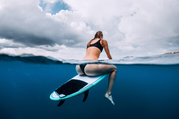 Surfer woman sitting on surfboard in clear blue ocean. Surf girl waiting wave.