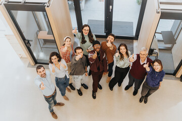 Aerial view of a happy, diverse group giving thumbs up in a modern office setting, showcasing...