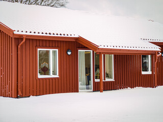 Old red wooden house in vintage Scandinavian style in winter. Traditional ancient Sweden house in the village. Snowy weather. 