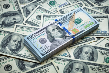 A stack of one hundred dollar bills against the backdrop of scattered dollars