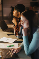 Two focused business coworkers working overtime in a dim office setup, analyzing data and planning strategies.