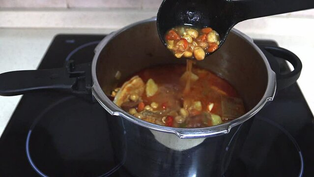 A hand with a saucepan in a pot with Andalusian chickpea stew, close-up. Slow motion. Spanish food concept.