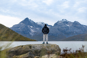 Persona contemplando montañas rocosas con nieve desde una roca a orillas de un fiordo