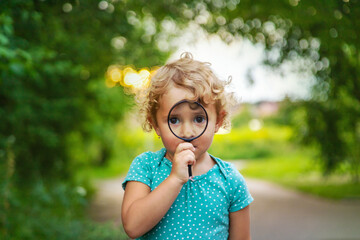 A child looks through a magnifying glass in nature. Selective focus.