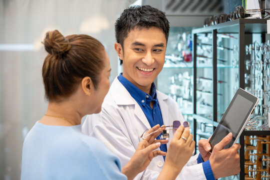 Young Asian male man optician explaining and selling eyeglasses to senior female woman customer in optical shop store. Eyecare concept.