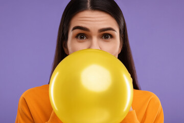 Woman inflating yellow balloon on purple background