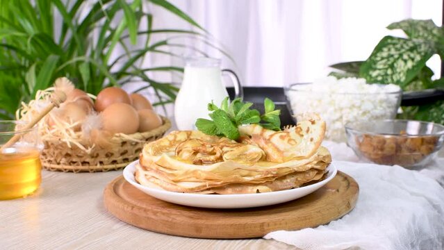Freshly baked homemade thin pancakes on a plate with honey and mint. One of a series of video recipes. Movement from left to right, close-up, real time.