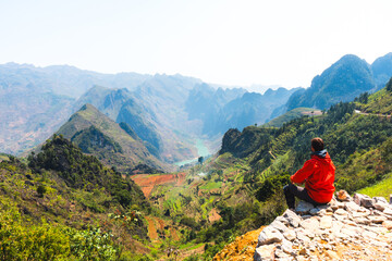 Naklejka premium A person in an orange jacket sitting and overlooking a scenic mountain valley