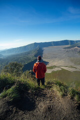 Naklejka premium A person in a red jacket admiring the vast expanse of a mountainous landscape.