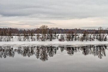 Winter landscape with river, forest at overcast weather.