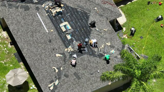 Workers laying asphalt shingles on new house rooftop. Roof finishing works on Florida home. Real estate development concept
