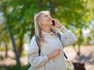 Young beautiful woman using smartphone in city park. Smiling female student texting on mobile phone outdoor. Modern lifestyle, connection, casual business concept