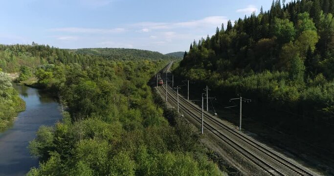 Freight long train carries with coal carriages on stone bridge by dangerous part of Trans Siberian railways near river in forest mountains. Aerial drone wide view at summer sunny sunset