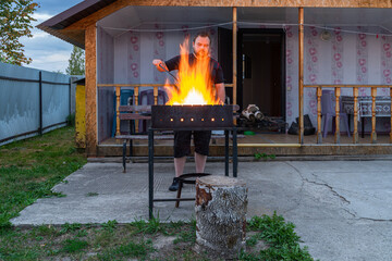 A young man 30-32 years old builds a fire with birch wood in a barbecue for grilling kebabs meat on...
