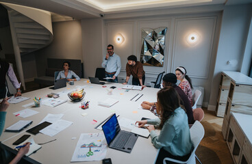 A multiethnic group of colleagues collaboratively working in a stylish office setting, surrounded...